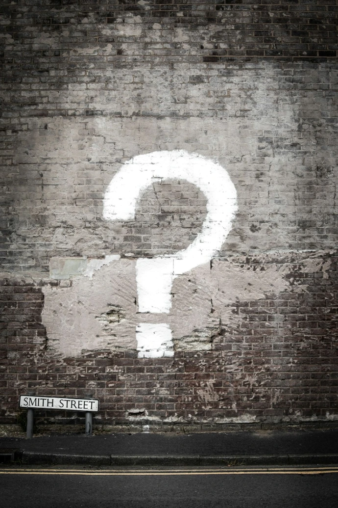 A large white question mark painted on a weathered brick wall above a street sign